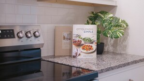Una cocina con estufa, un libro de cocina titulado 'Ottolenghi Simple' y una planta en maceta.