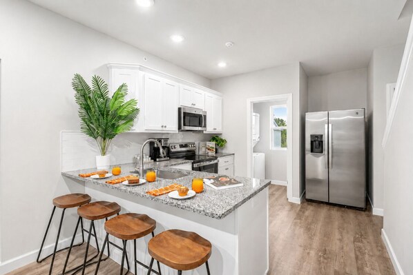 A modern kitchen with white cabinets, stainless steel appliances, a granite countertop, and a bar area with stools.
