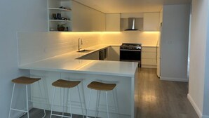 Uma cozinha moderna com uma ilha central, banquetas, forno embutido e painel de parede branco.