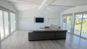 Uma sala de estar espaçosa com um sofá seccional grande, uma TV de tela plana na parede e grandes portas de vidro deslizantes que dão para uma varanda.