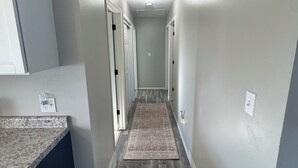 Um corredor estreito com piso de madeira, paredes brancas e luminária no teto.
