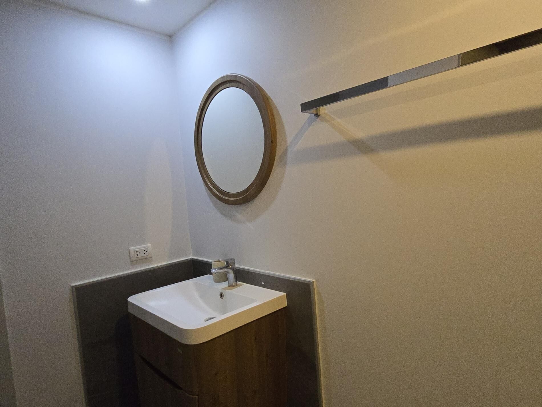 Een badkamer met een witte wastafel, een ronde spiegel en een handdoekhouder.