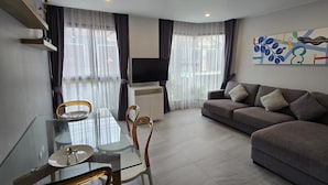 Een moderne woonkamer met een glazen eettafel, een grijze bank en een flatscreen televisie.