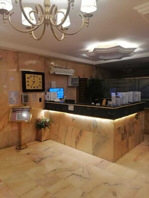 A reception area with a marble counter, a clock, an air conditioning unit, and a chandelier. - fakhamat almasif (Taif)