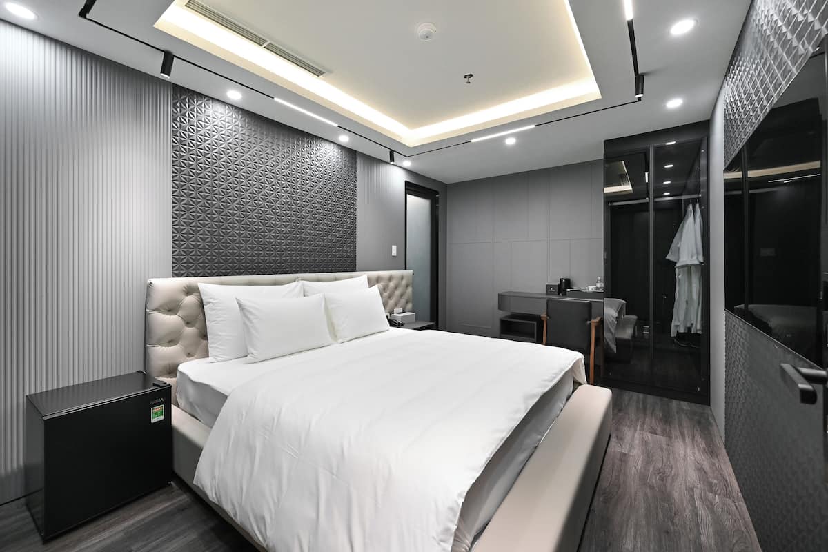 Une chambre moderne dotée d’une tête de lit capitonnée, d’une table de chevet, d’un grand lit, d’un dressing et d’une douche en verre.