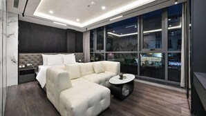 A modern hotel room with a sectional sofa, a round coffee table, and a large window offering a city view. - Accord Hotel Binh Tan (Ho Chi Minh City)
