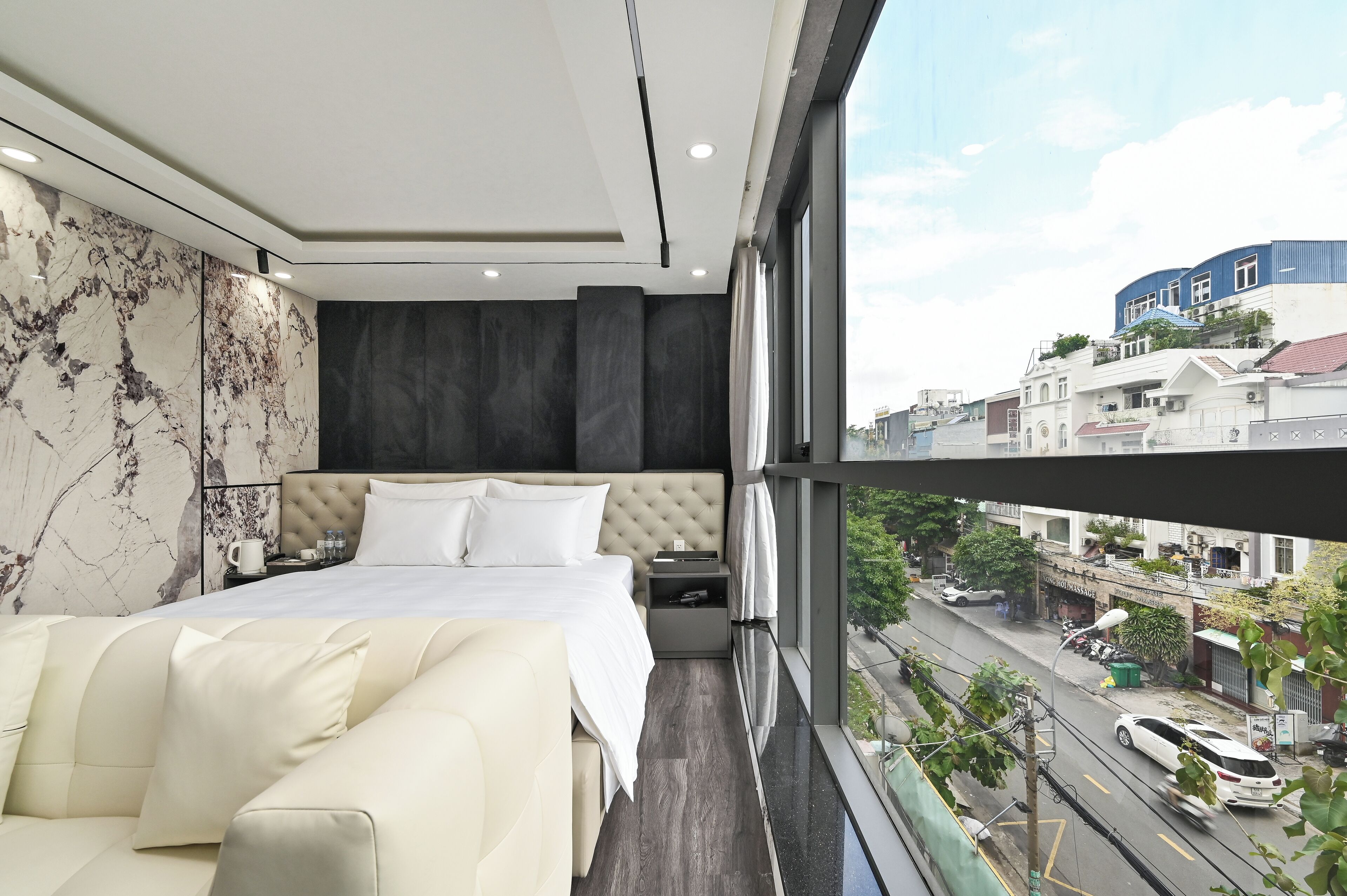 Quarto de hotel moderno com uma cama grande, um sofá e vista da cidade por grandes janelas.