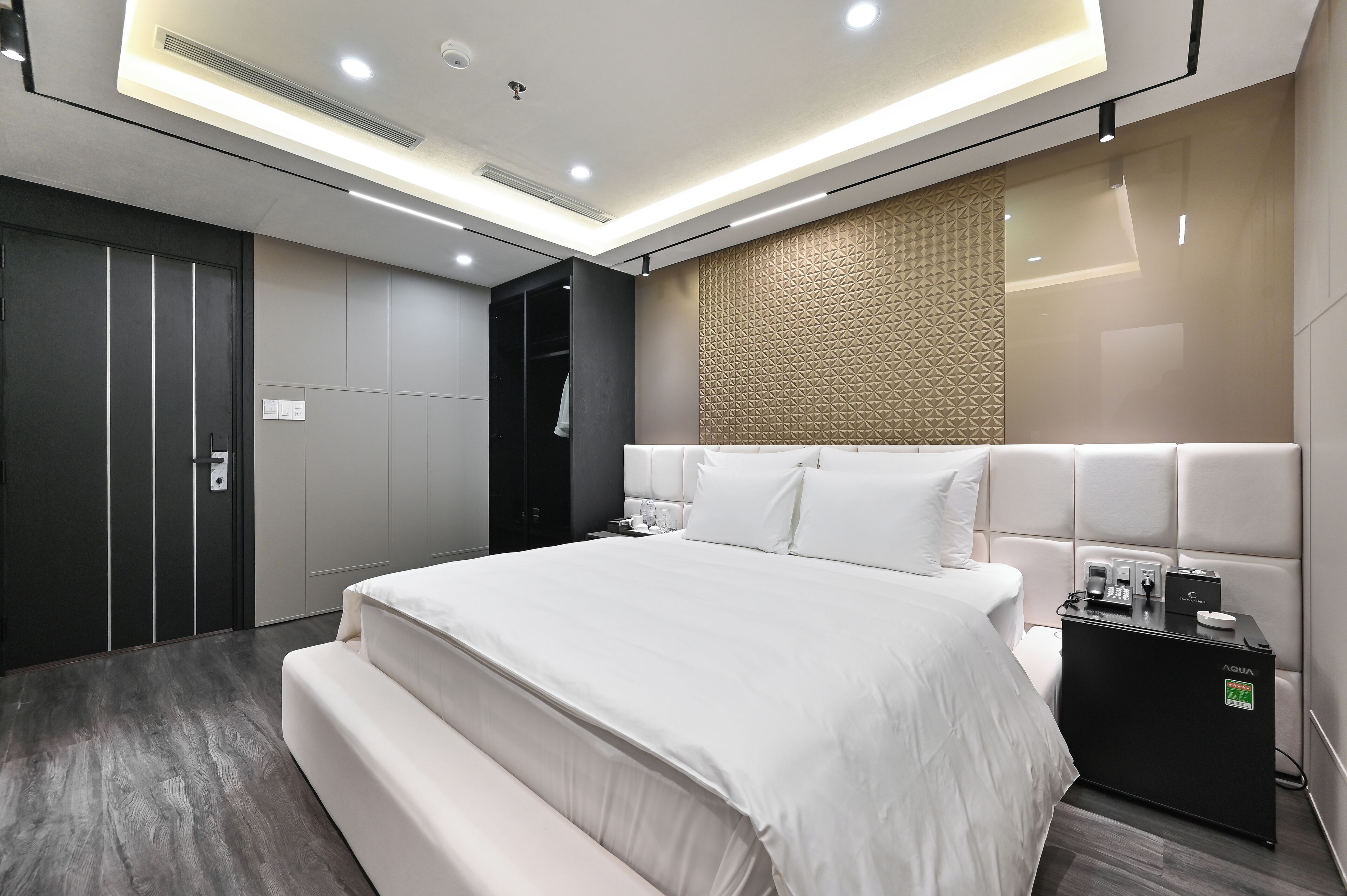 Una habitación de hotel moderna con una cama grande, armario empotrado, minibar y un diseño de pared con textura.