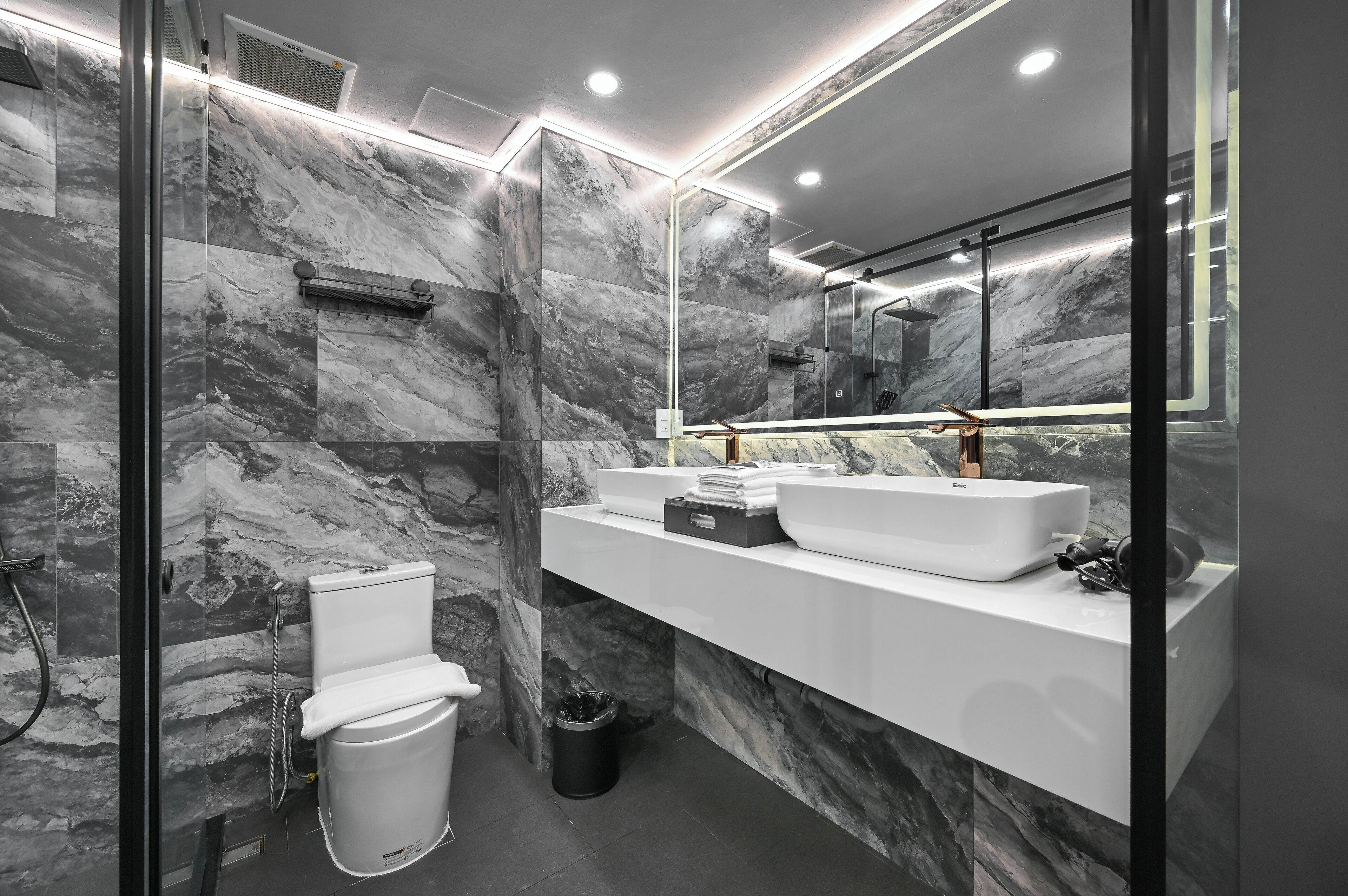 Un baño moderno con paredes de mármol, un lavabo blanco y un box de ducha de vidrio.