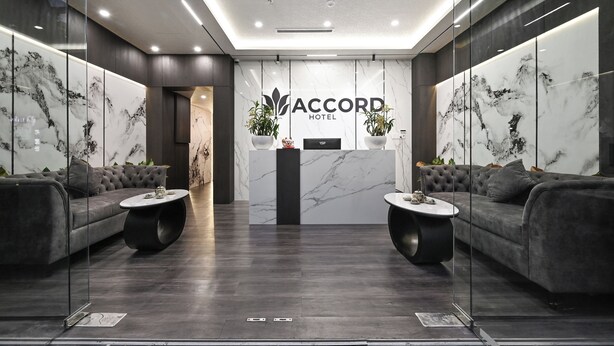 A modern hotel lobby with marble walls, dark wood flooring, and two sofas with round coffee tables. - Accord Hotel Binh Tan (Ho Chi Minh City)