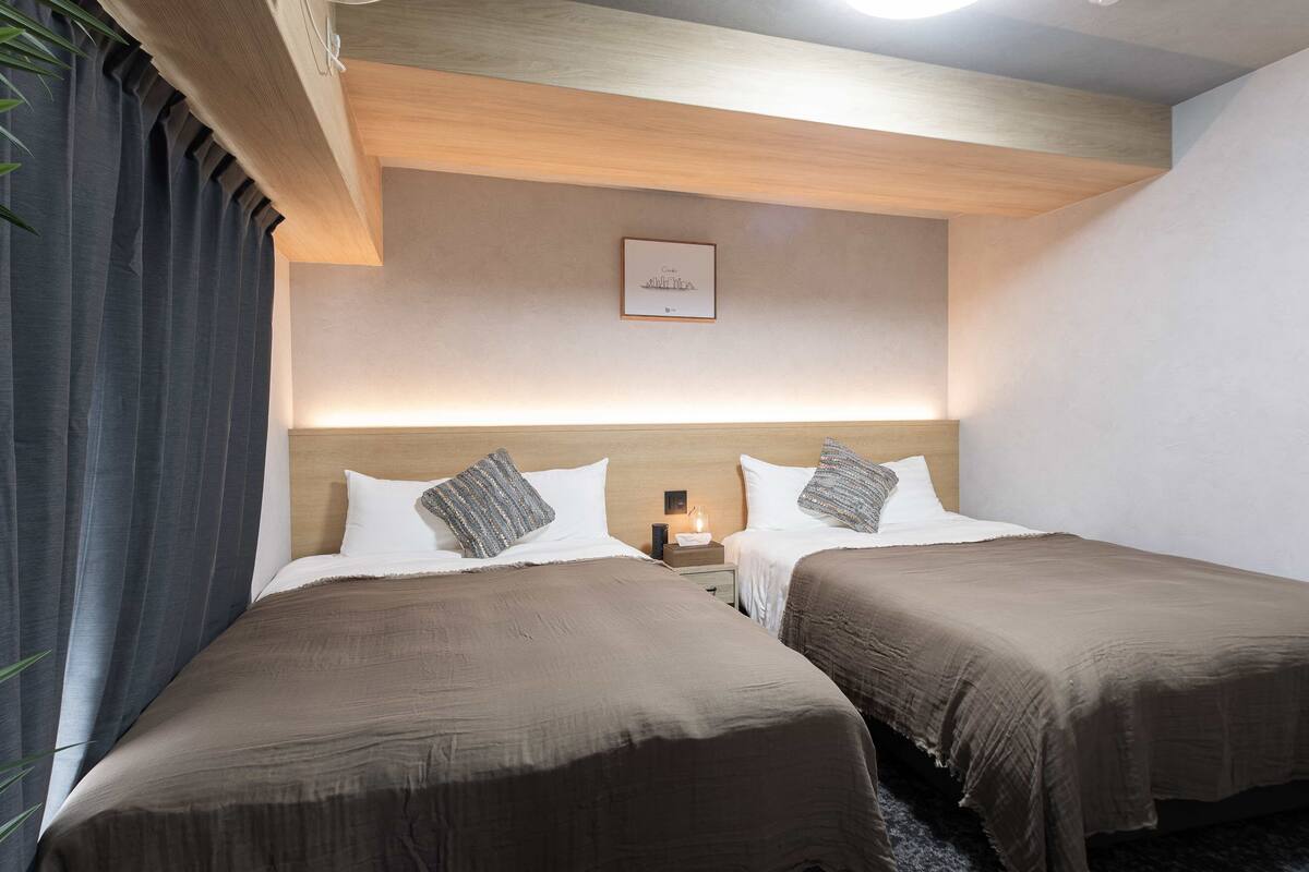 Camera d'albergo con due letti, soffitto in legno, un quadro appeso al muro e un comodino con una lampada.