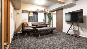 Un espace de vie compact comprenant un canapé, un banc, une table à manger et un téléviseur posé sur un meuble.