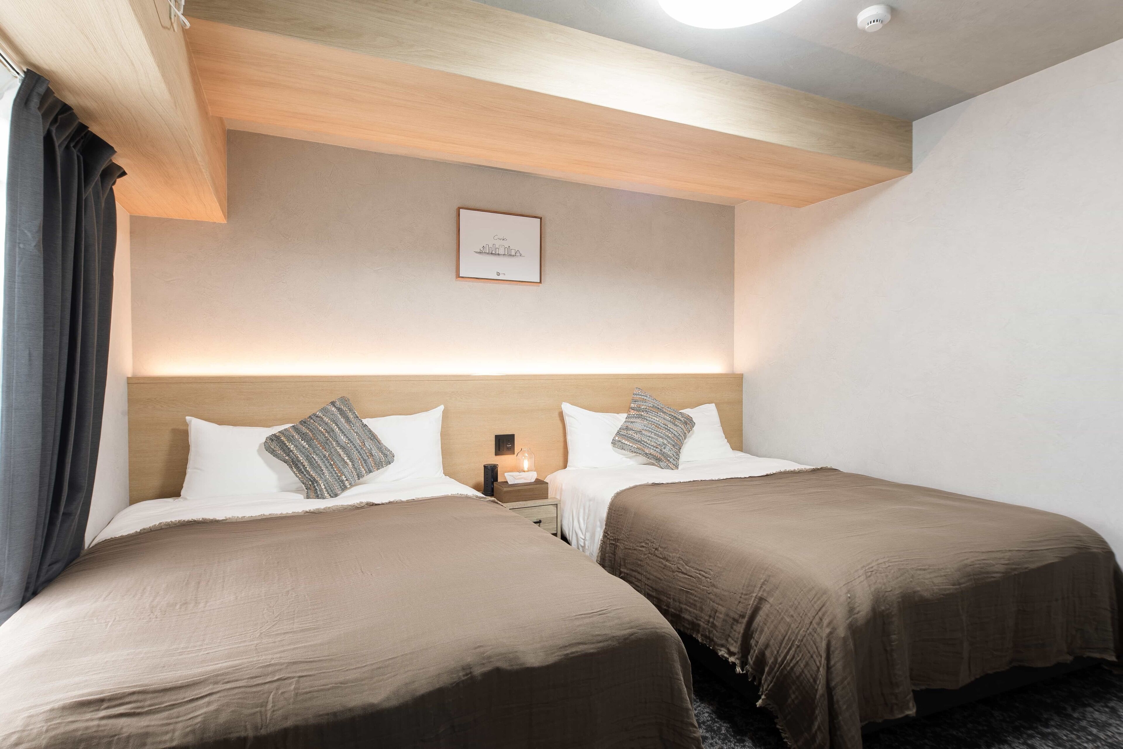 A hotel room with two beds, a nightstand, a framed picture on the wall, and a ceiling light.