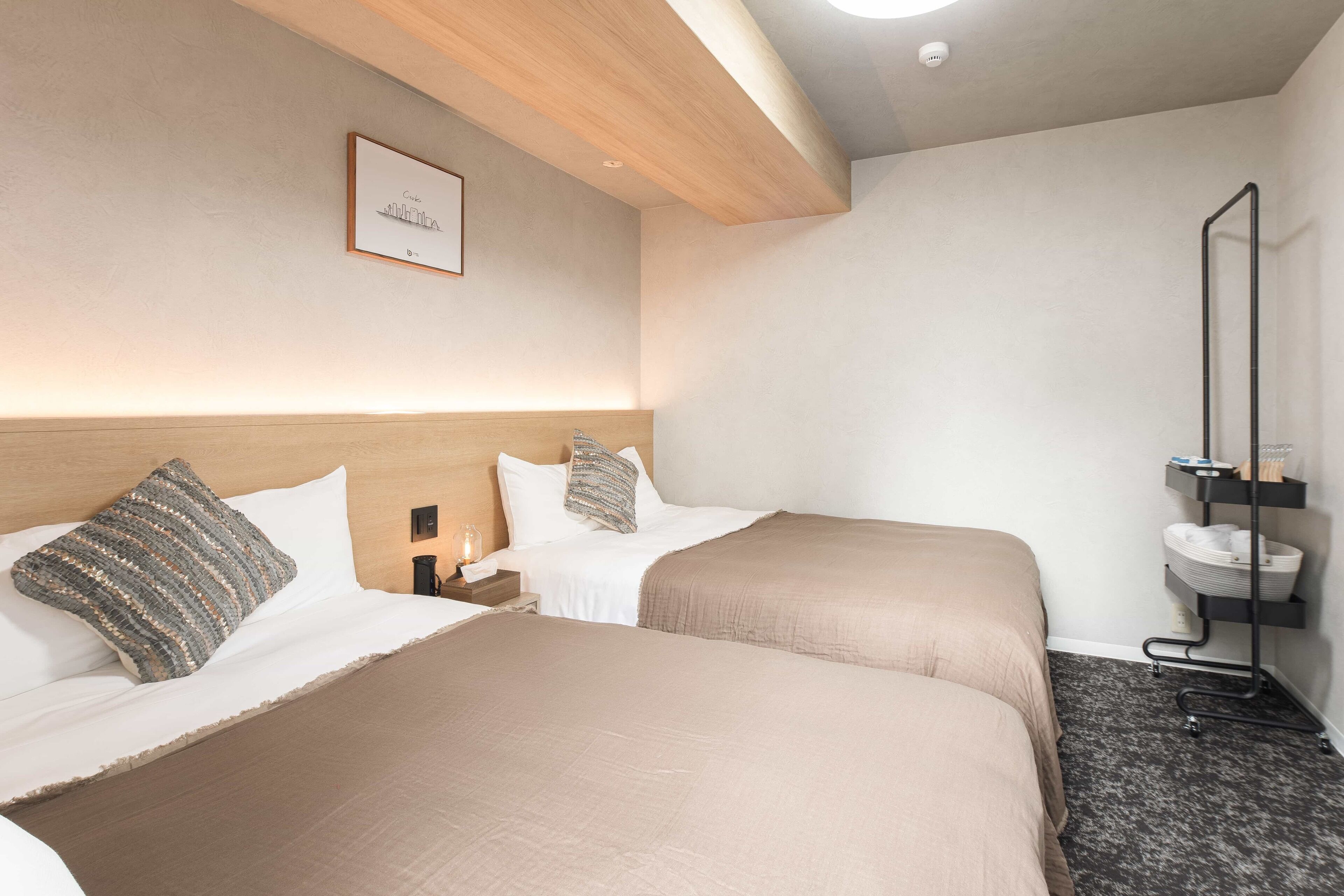 A hotel room with two beds, a bedside table, a nightstand, a framed picture on the wall, and a bathroom with a sink and mirror.