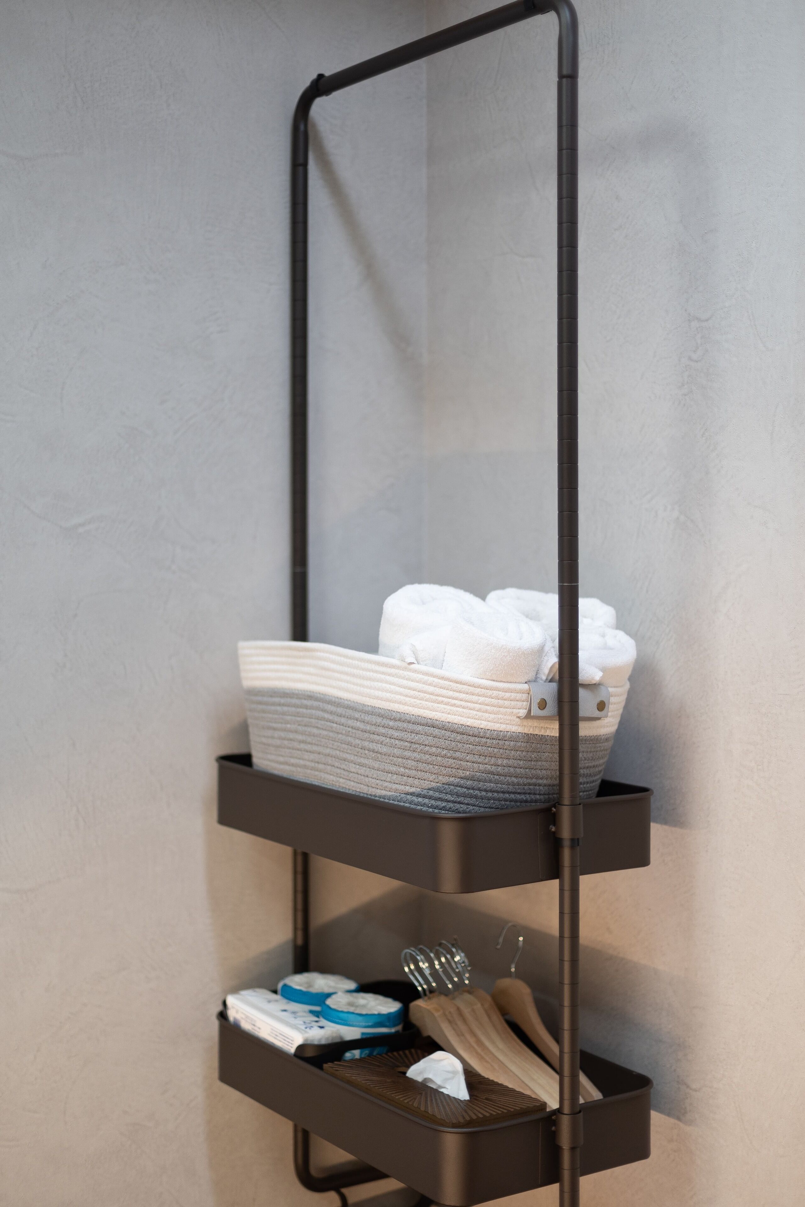 A black metal shelf unit with towels and toiletries against a textured wall.