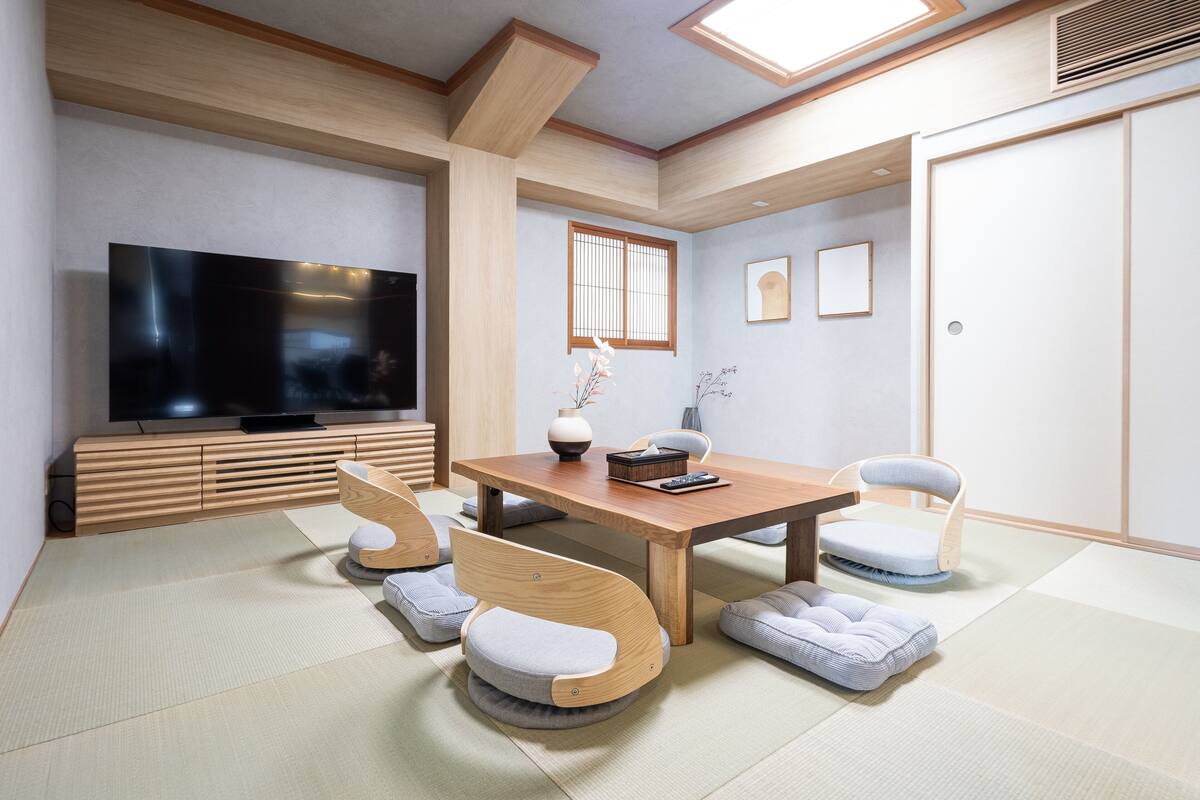 Un soggiorno moderno con un tavolo da pranzo in legno, poltrone imbottite, una televisione a schermo piatto e tatami.