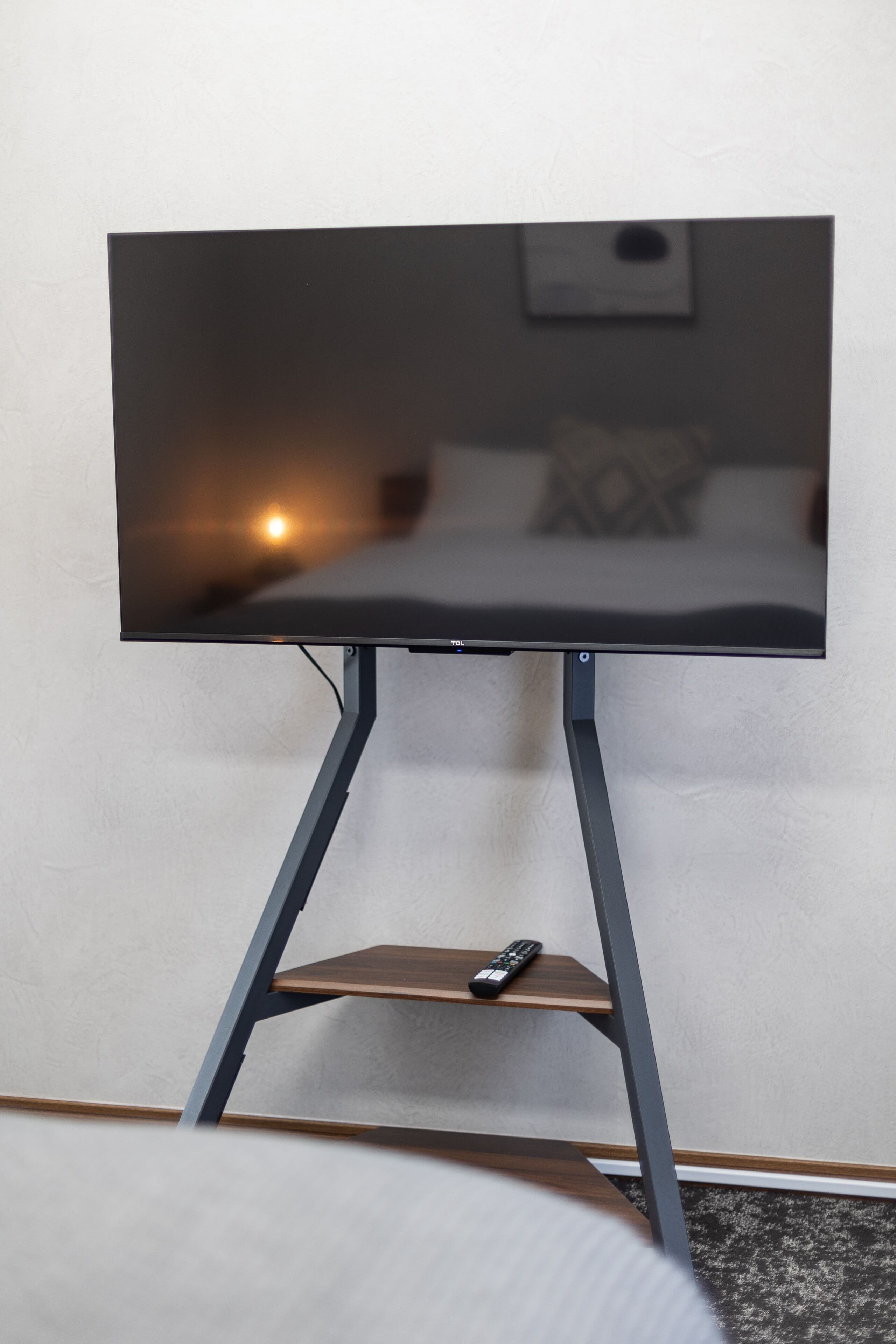 Moderni televisio, joka on sijoitettu jalustalle, ja sen kaukosäädin on hyllyllä.
