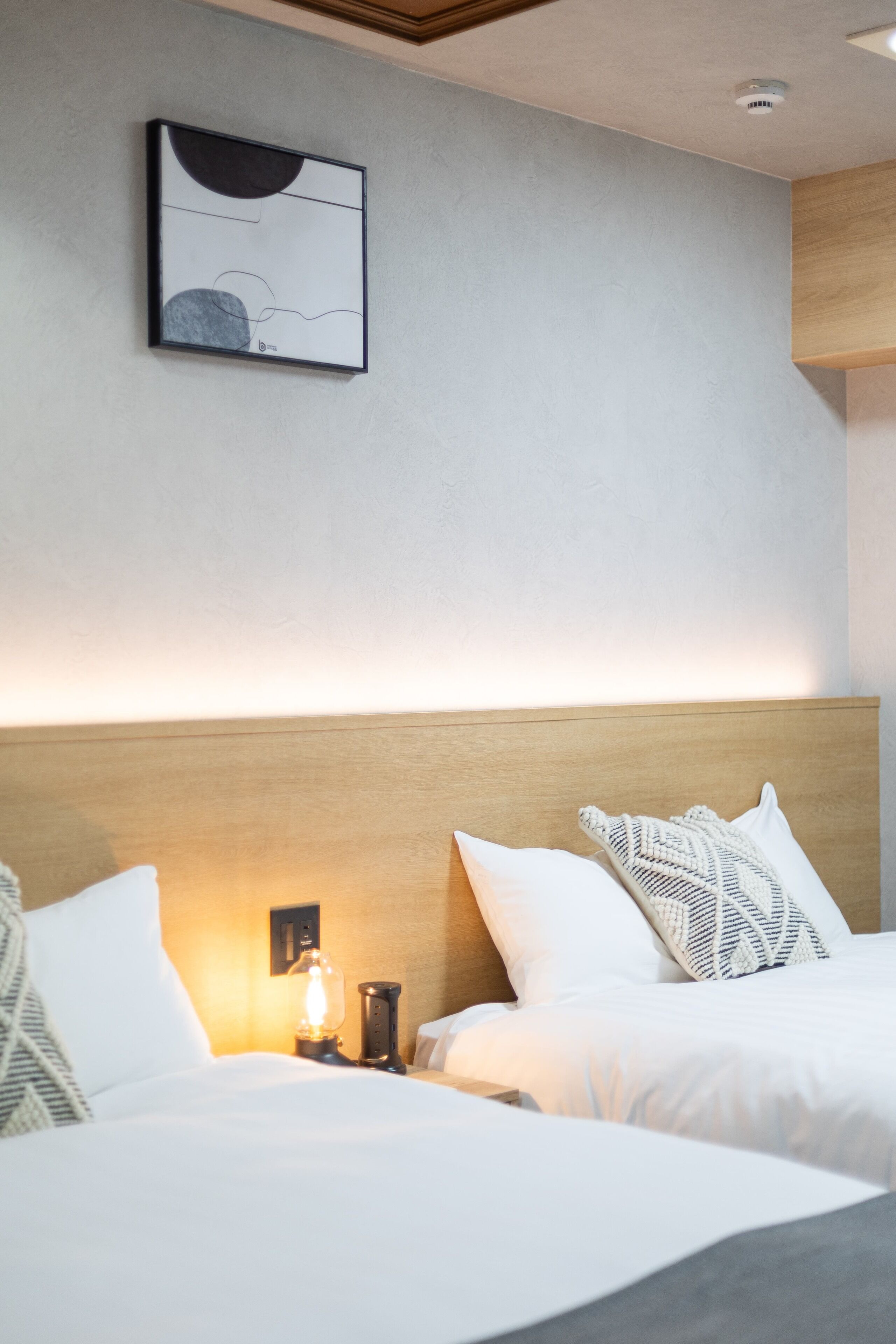 Habitación de hotel con dos camas, cabecero de madera, una obra de arte colgada en la pared y una mesita de noche con lámpara.