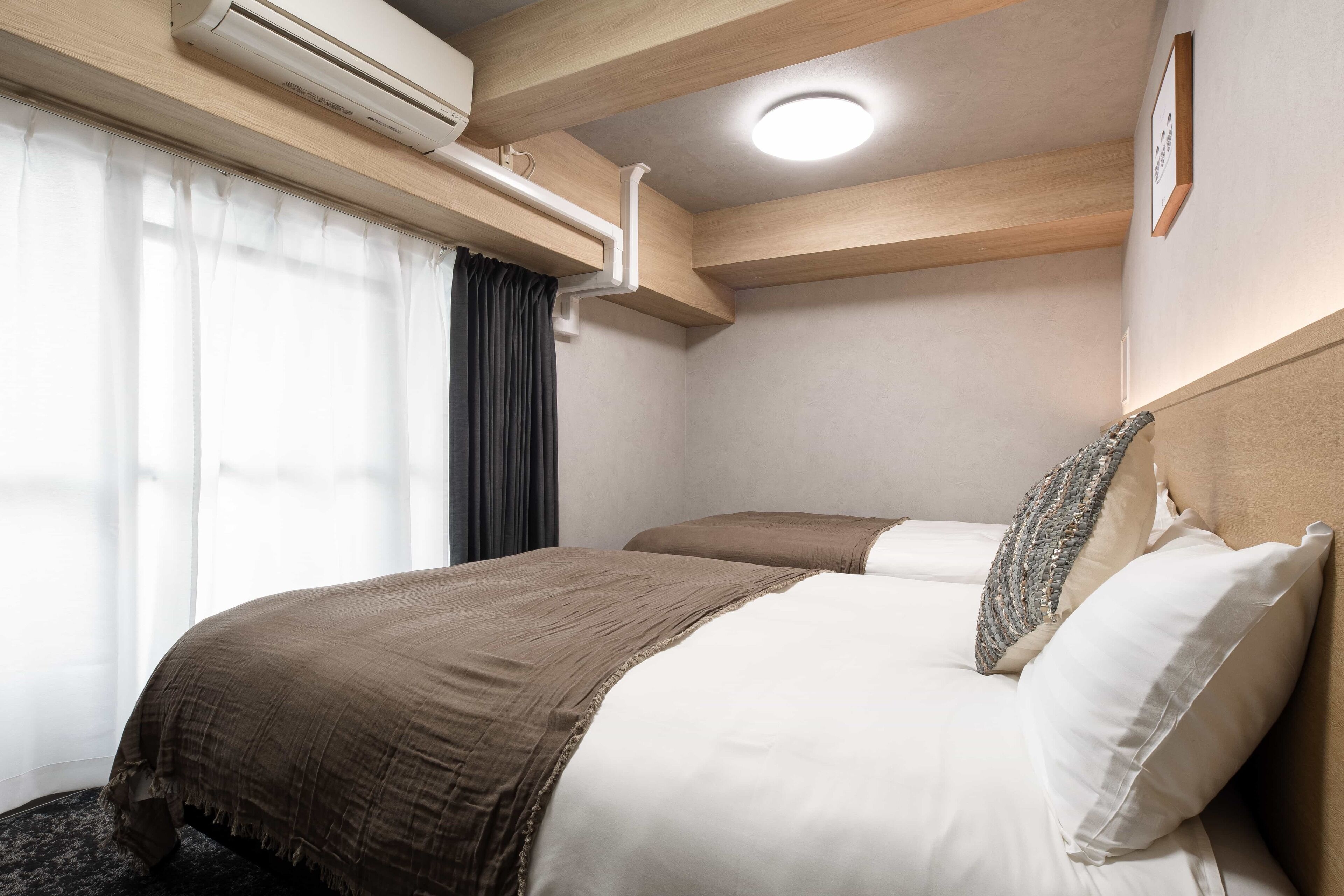 Quarto de hotel com cama, janela com cortinas, ar condicionado e luminária no teto.