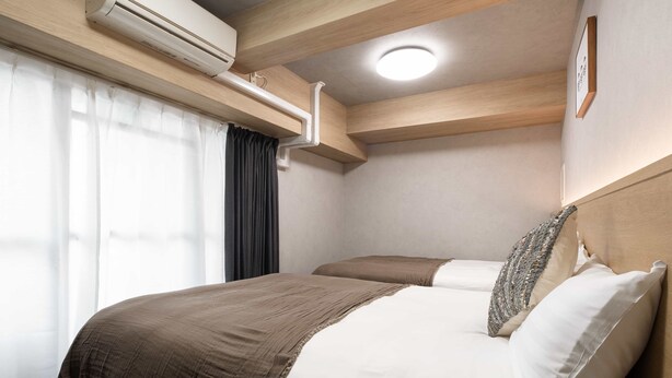 A hotel room with a bed, a window with curtains, an air conditioning unit, and a ceiling light. - b&Namba1 (Osaka)