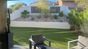 Un espace patio aménagé avec du mobilier d’extérieur, une pelouse bien entretenue et un mur décoratif en pierres agrémenté de plantes.