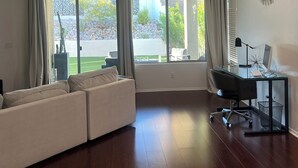 Un salon spacieux doté d’une grande fenêtre, d’un ventilateur de plafond, d’un fauteuil de bureau noir et d’un bureau en verre.