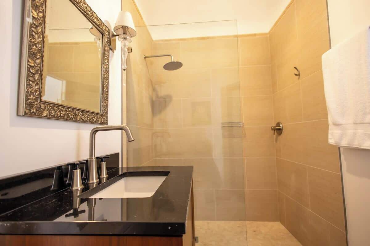 A bathroom with a black countertop sink, a large ornate mirror, and a glass-enclosed shower.