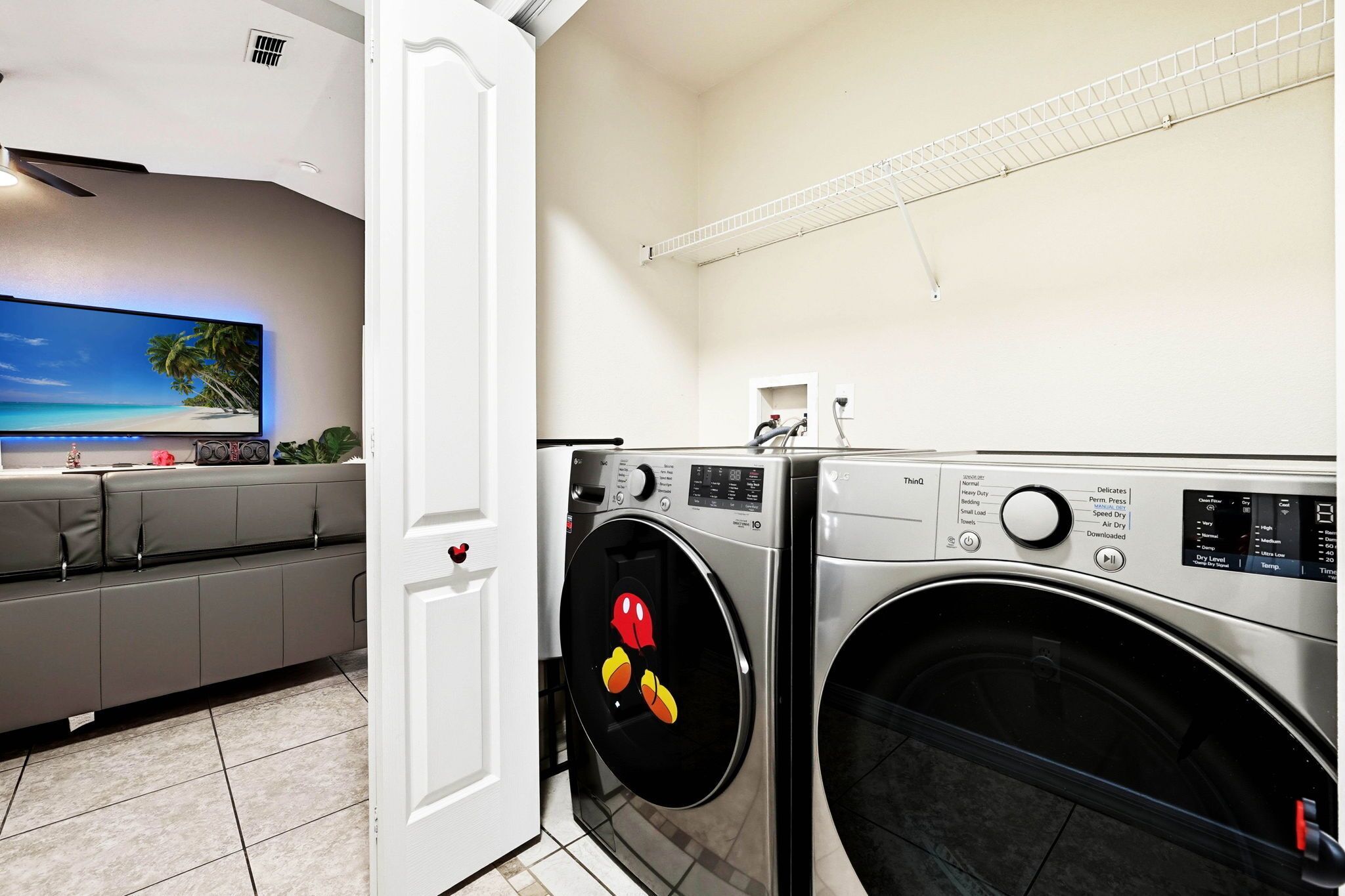 A laundry room with a washing machine and dryer, a television mounted on the wall, and a seating area with a sofa.
