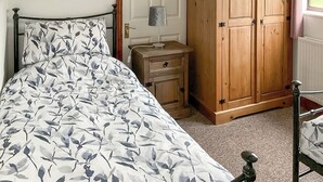 A bedroom with a bed, a nightstand, a wooden wardrobe, and a window. - Mistletoe Cottage - UK50581 (Burnham-on-sea)