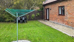 A backyard with a green drying rack, a brick house, and a stone pathway. - Mistletoe Cottage - UK50581 (Burnham-on-sea)
