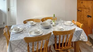 A dining table set with white plates, bowls, and glasses, surrounded by wooden chairs. - Mistletoe Cottage - UK50581 (Burnham-on-sea)