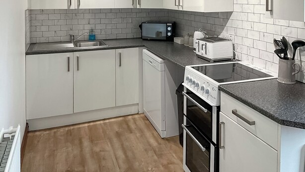 A modern kitchen with white cabinets, a black countertop, a microwave, a toaster, and a coffee maker. - Mistletoe Cottage - UK50581 (Burnham-on-sea)
