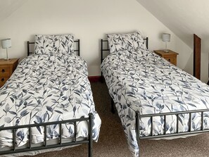 A twin bedroom with two single beds, each with a floral-patterned duvet, a bedside table with a lamp, and a wooden nightstand.