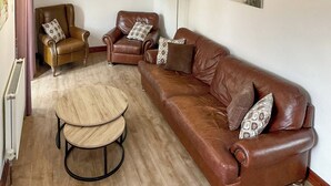A living room with a brown leather sofa, two armchairs, a round wooden coffee table, and a floor lamp. - Mistletoe Cottage - UK50581 (Burnham-on-sea)