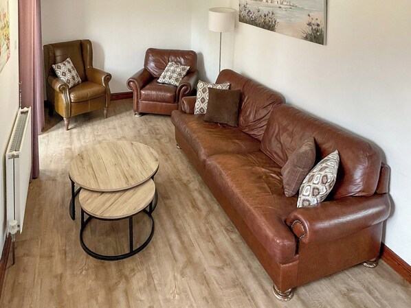 A living room with a brown leather sofa, two armchairs, a round wooden coffee table, and a floor lamp.