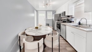 A modern kitchen with white cabinetry, a marble countertop, and a round dining table with chairs.