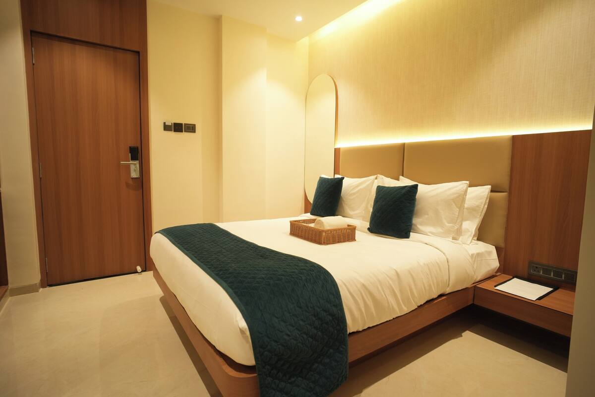 A modern hotel room with a large bed, a bedside table, a nightstand, and a wooden door.