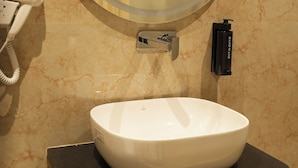 A bathroom with a round mirror, a white sink, a hairdryer, and a black soap dispenser. - The Jeevan Inn (Shirdi)