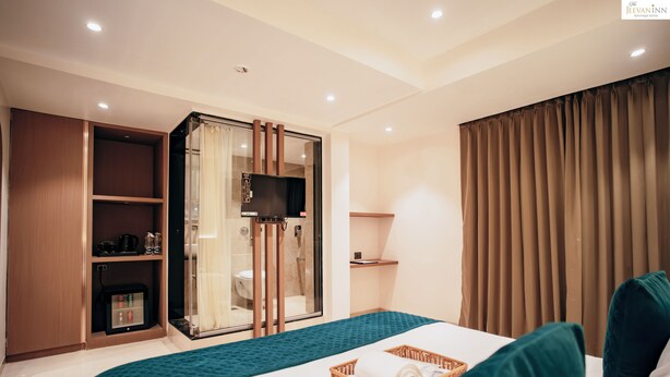 A hotel room with a bed, a wardrobe, a shower area, and a television. - The Jeevan Inn (Shirdi)