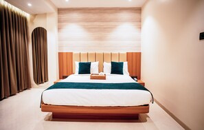 A modern hotel room with a large bed, wooden headboard, and a neutral color scheme.