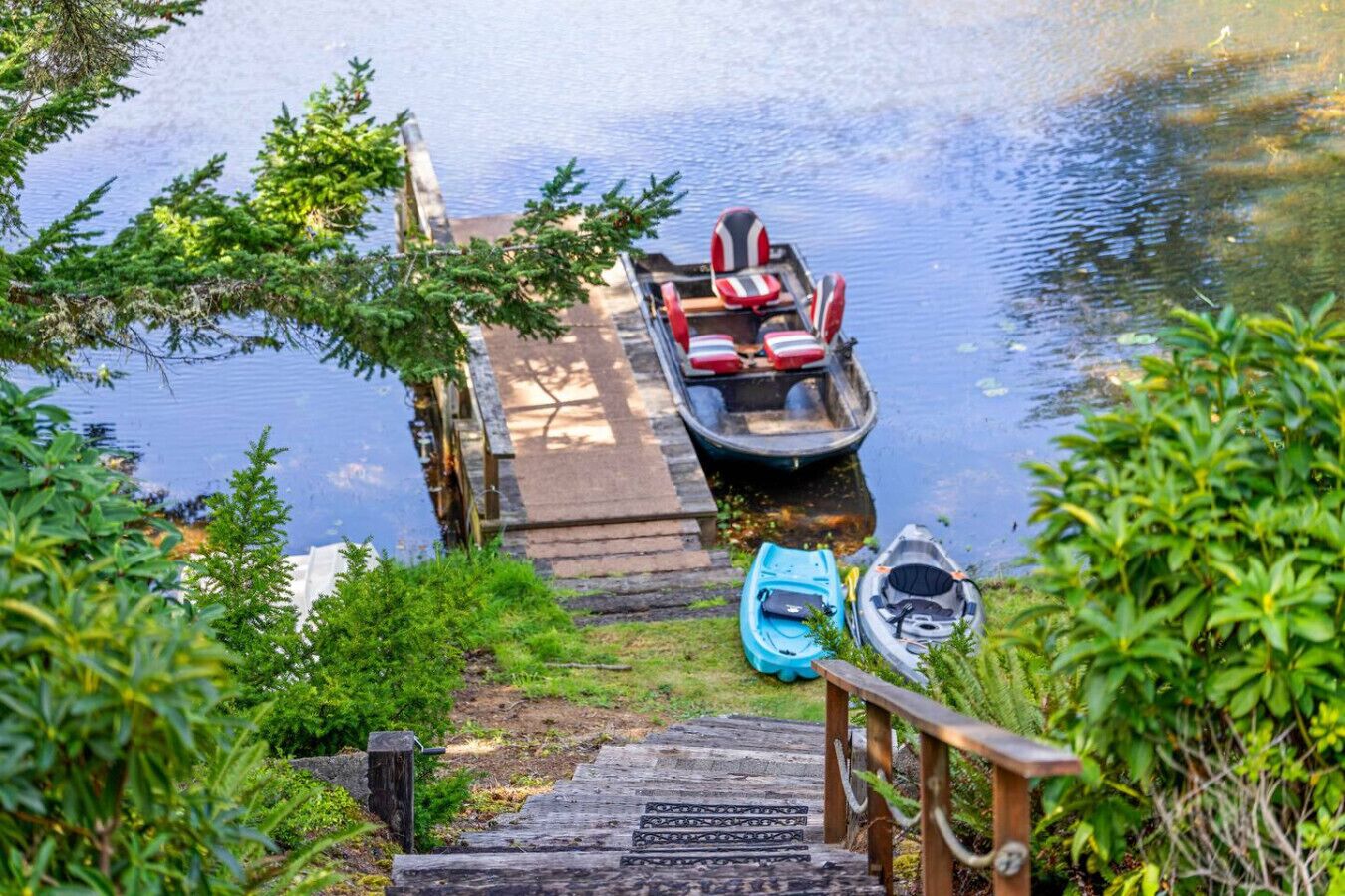 Un moll de fusta que condueix a un llac tranquil amb dues embarcacions, una amb coixins vermells i l'altra amb una funda blava.