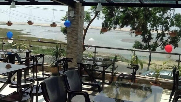 An outdoor seating area with tables and chairs, potted plants, and a view of a body of water. - Sampan Resort (Cox's Bazar)
