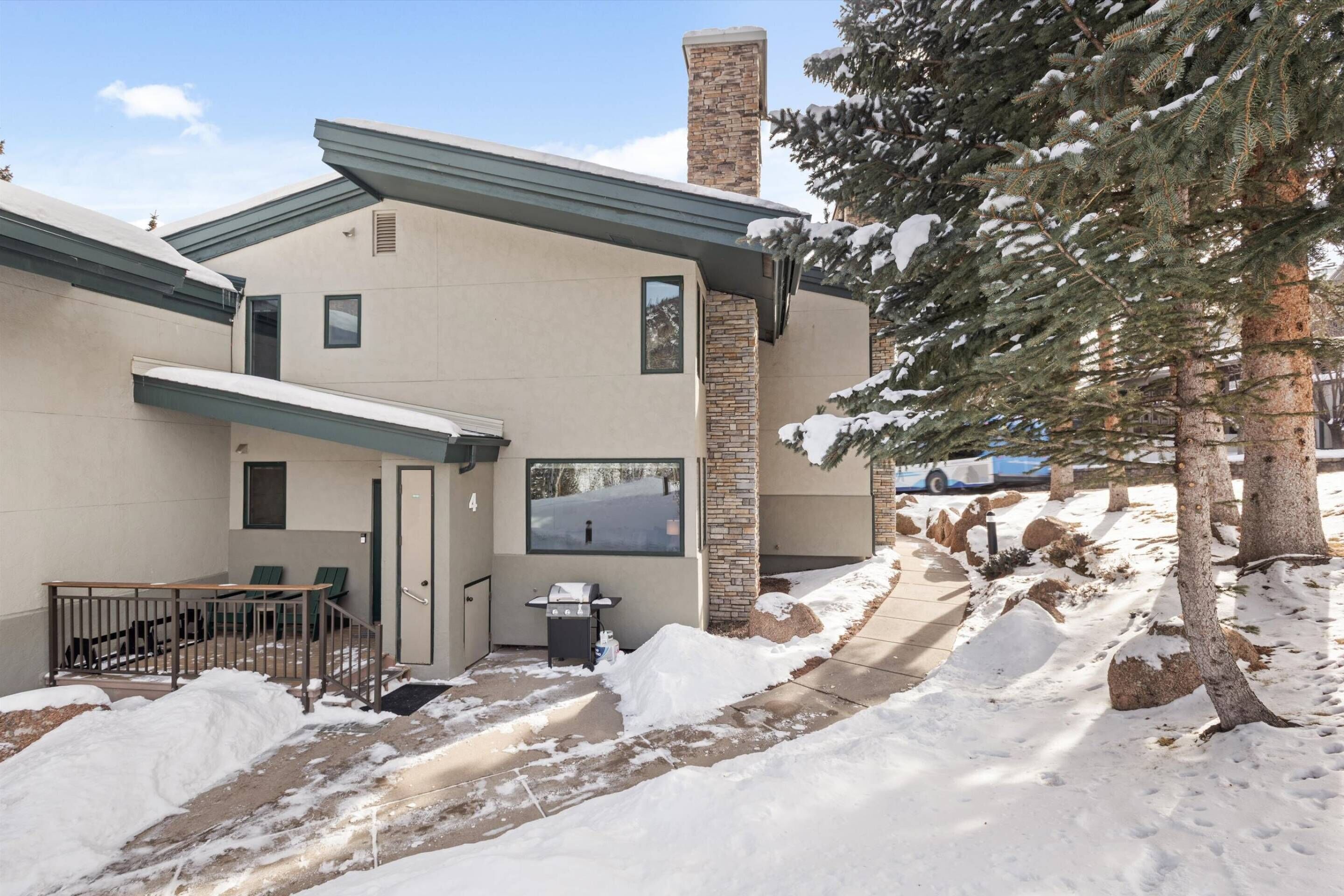 A modern building with a stone chimney, a covered patio with outdoor seating, and a snow-covered landscape.