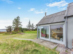 Une maison moderne avec une extension en verre, un chemin en pierre et une cour gazonnée.