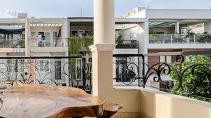 Un ampio balcone con tavolo da pranzo in legno, colonne bianche e vista sui palazzi vicini.