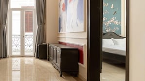 Camera d'albergo con un letto grande, un comodino, una cassettiera e vista su un'altra stanza attraverso una porta aperta.