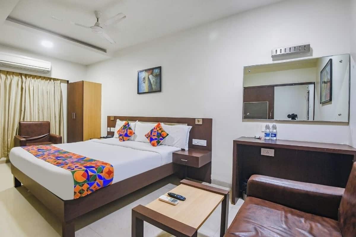 A hotel room with a bed, a desk, a chair, a wardrobe, a mirror, and an air conditioning unit.