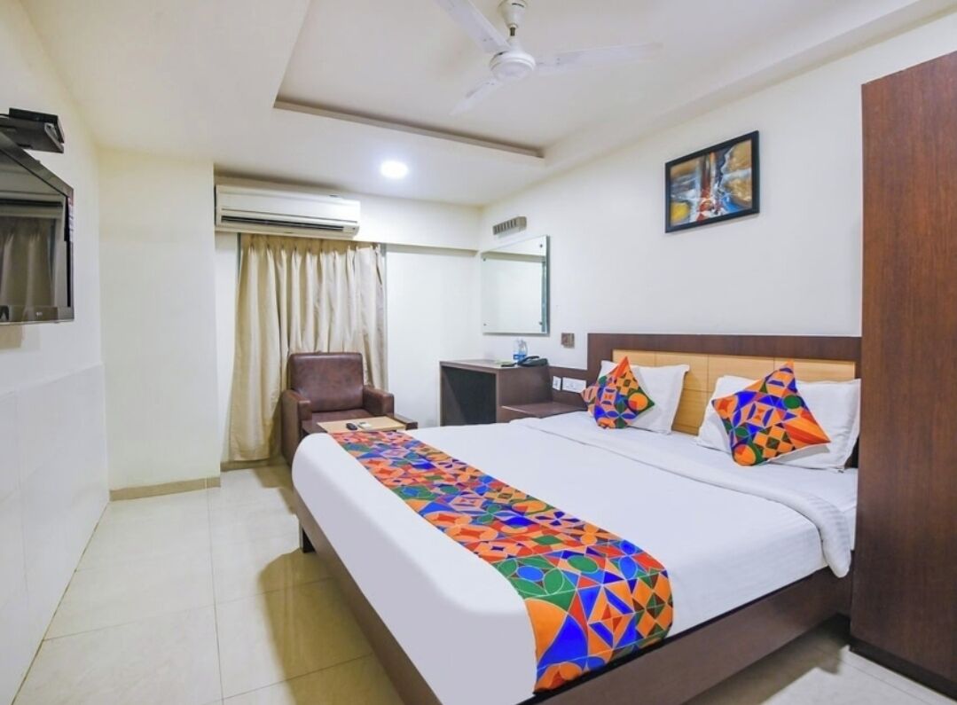 Una habitación de hotel con cama, una silla, un escritorio, unidad de aire acondicionado, ventilador de techo y un cuadro en la pared.