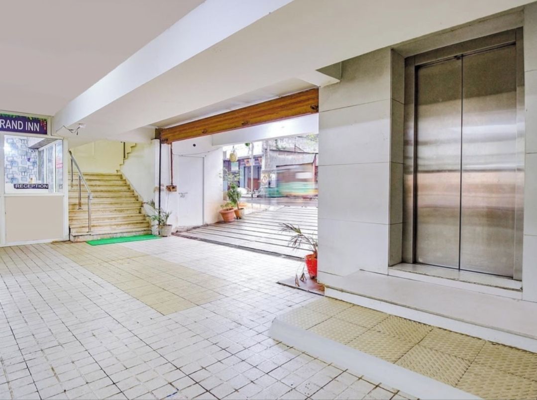 A hotel reception area with a staircase leading to the upper floors, a reception desk, and a large sliding door.