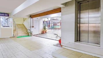 A hotel reception area with a staircase leading to the upper floors, a reception desk, and a large sliding door.